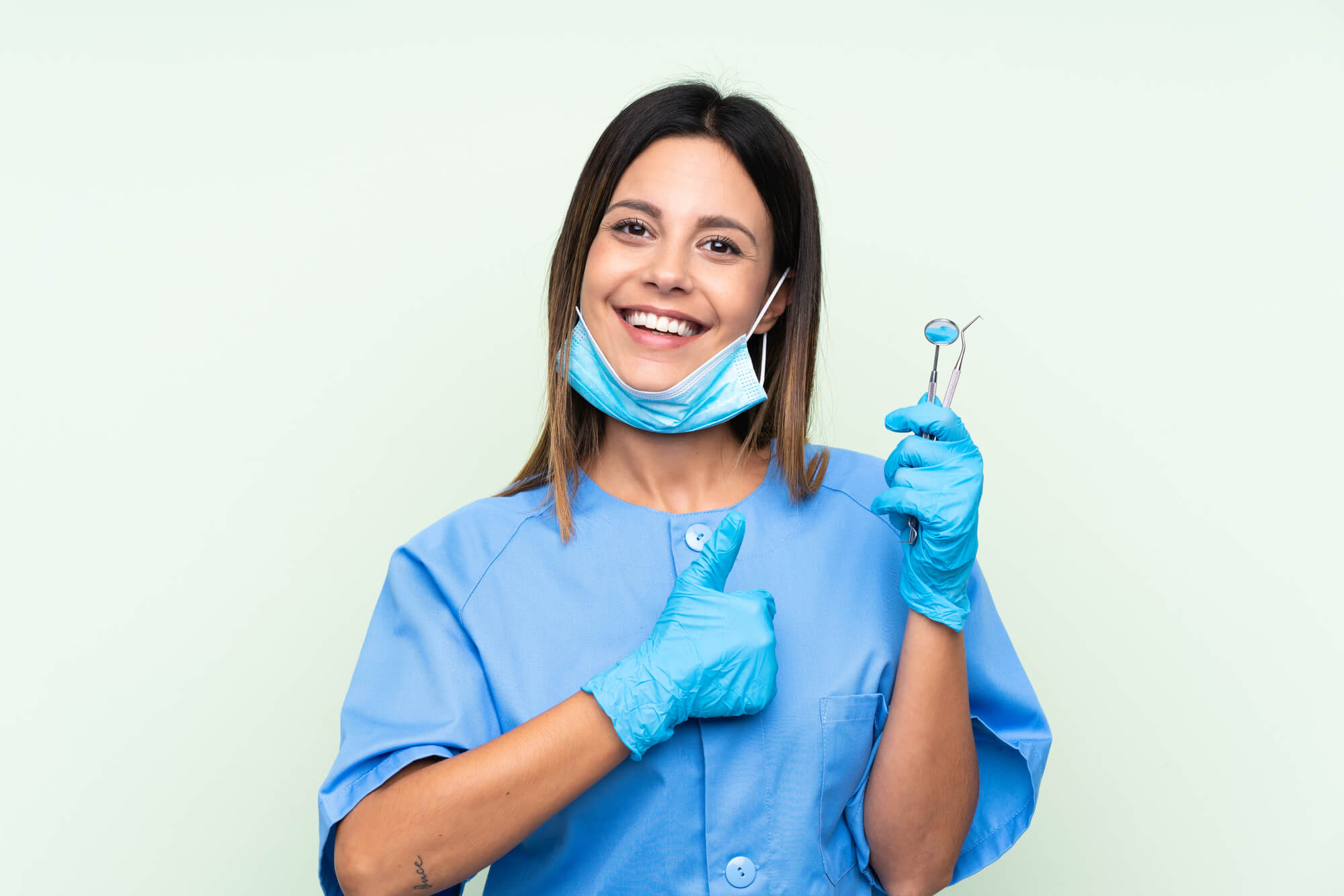 female dentist giving thumbs up in one hand and holding tools in another