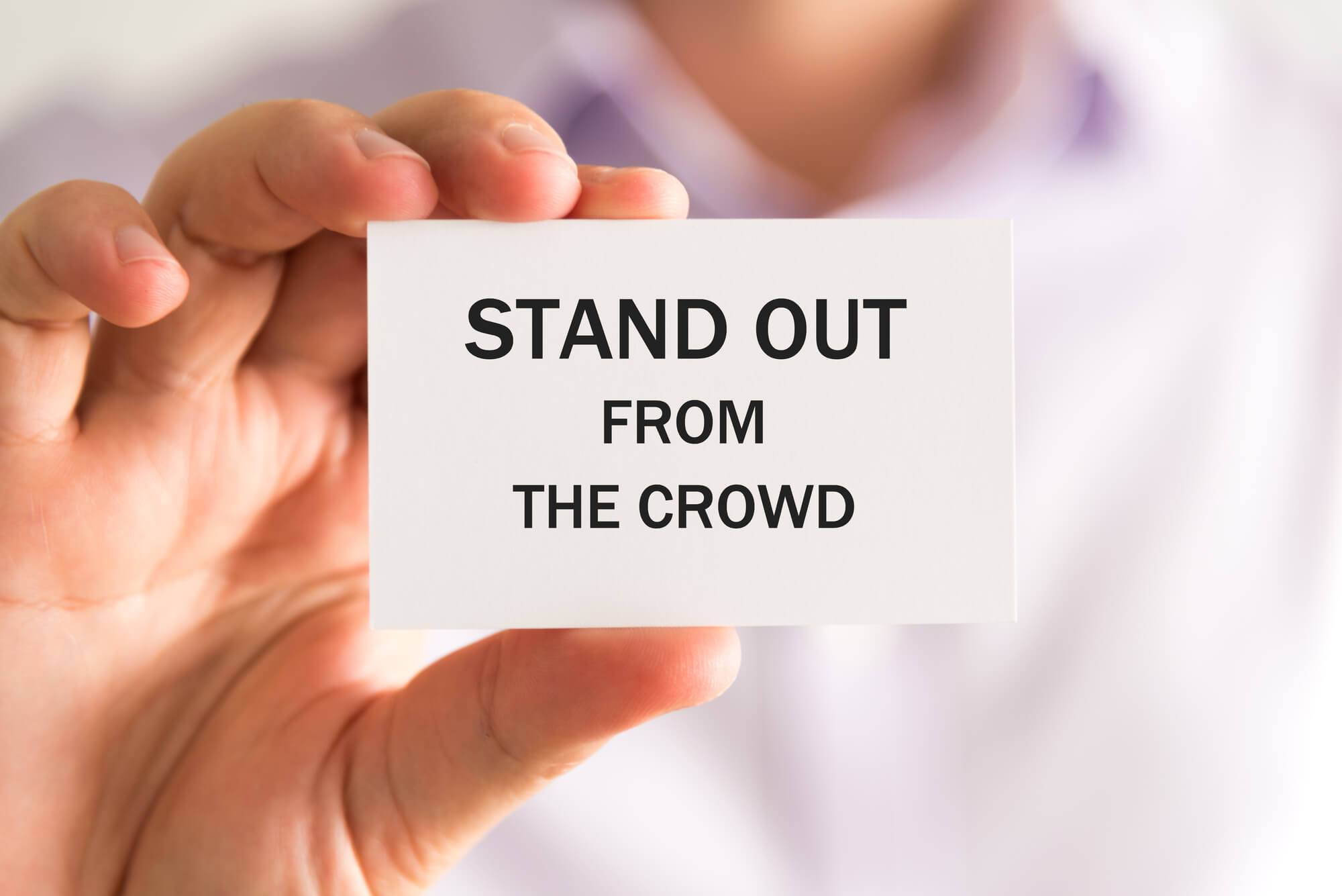 man holding note that says stand out from the crowd