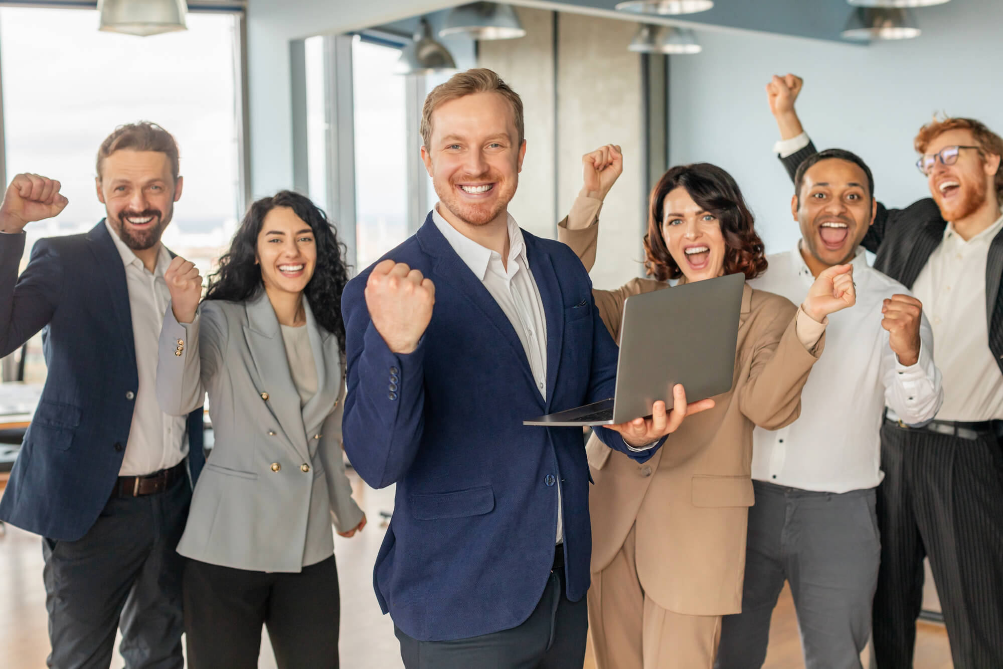 a cheerful team celebrates success, with the leader holding a laptop and others raising their fists in excitement