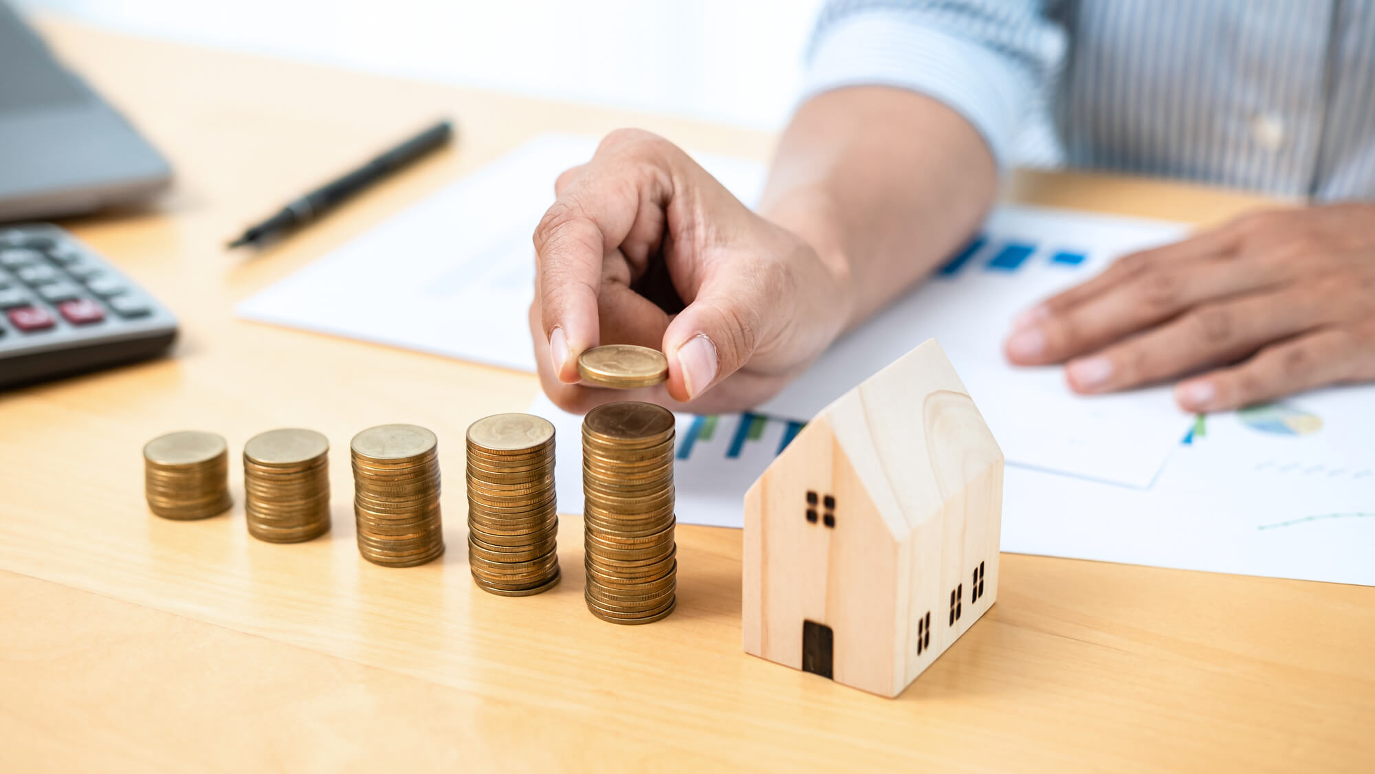 businessman stacking coins beside a small wooden house model