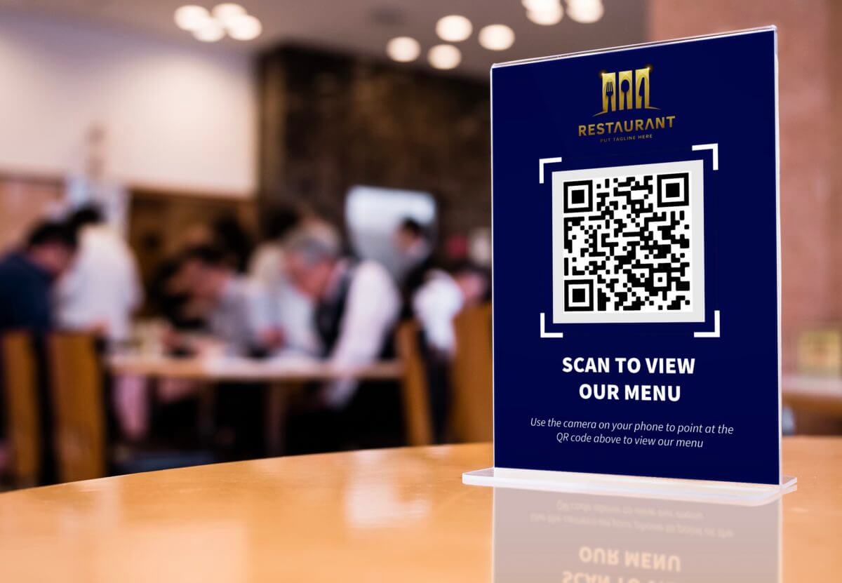 a dark blue table tent card with a QR code and the text "Scan to view our menu" sits on a restaurant table