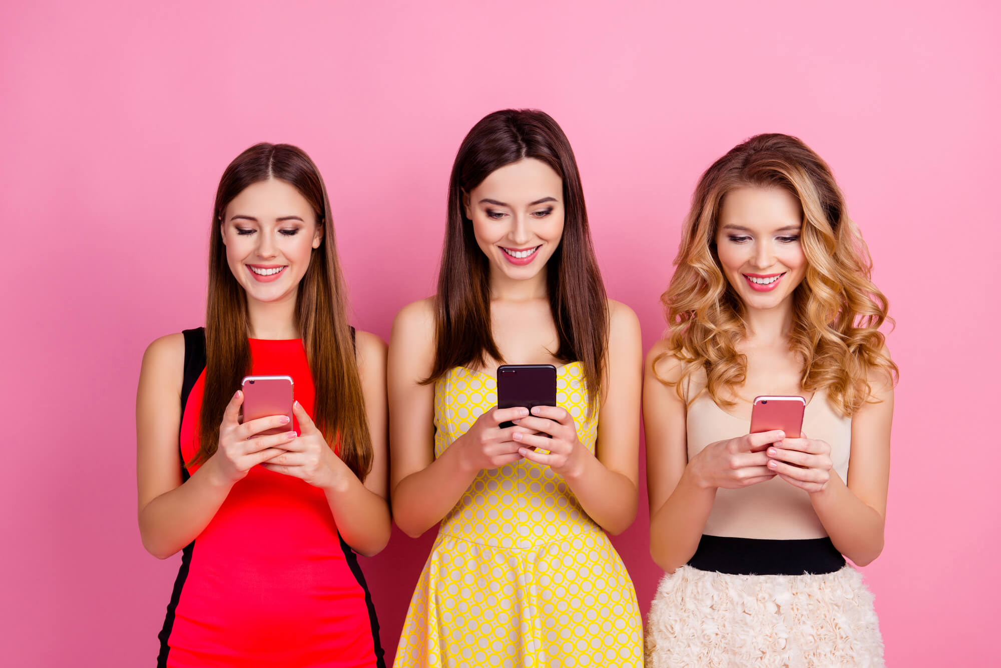 three young women focusing on their phones while smiling
