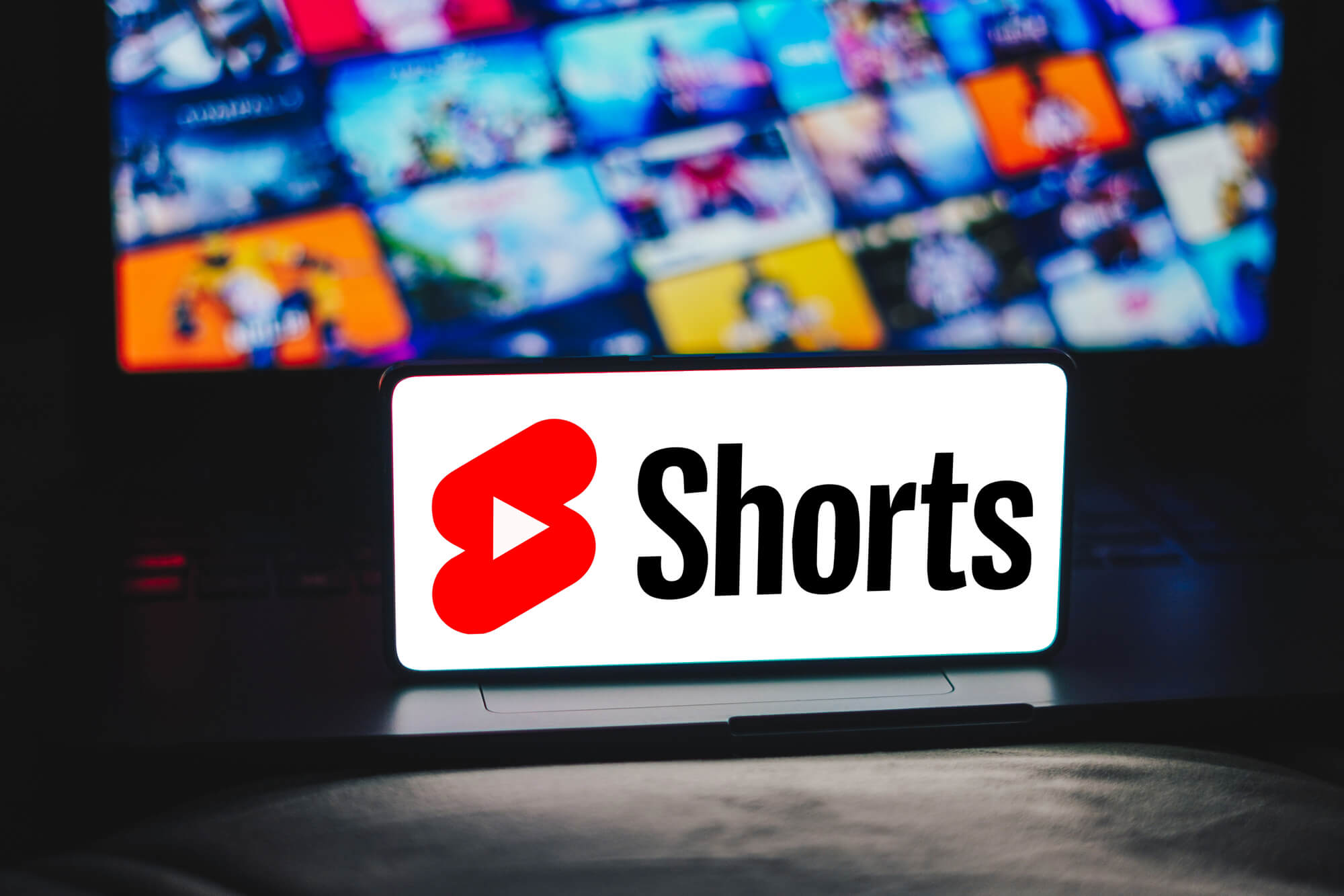 phone displaying shorts with laptop behind showing video clips