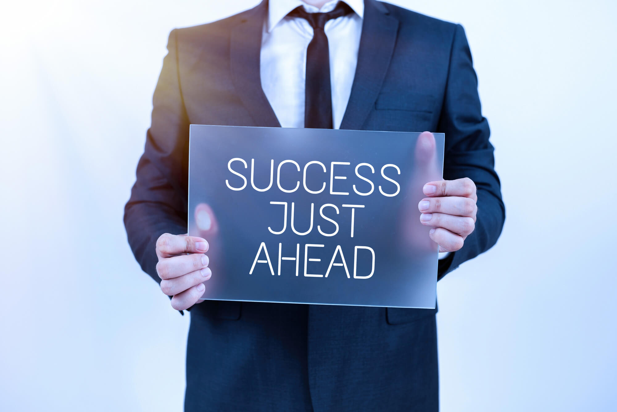 male professional holding a sign that reads "SUCCESS JUST AHEAD"