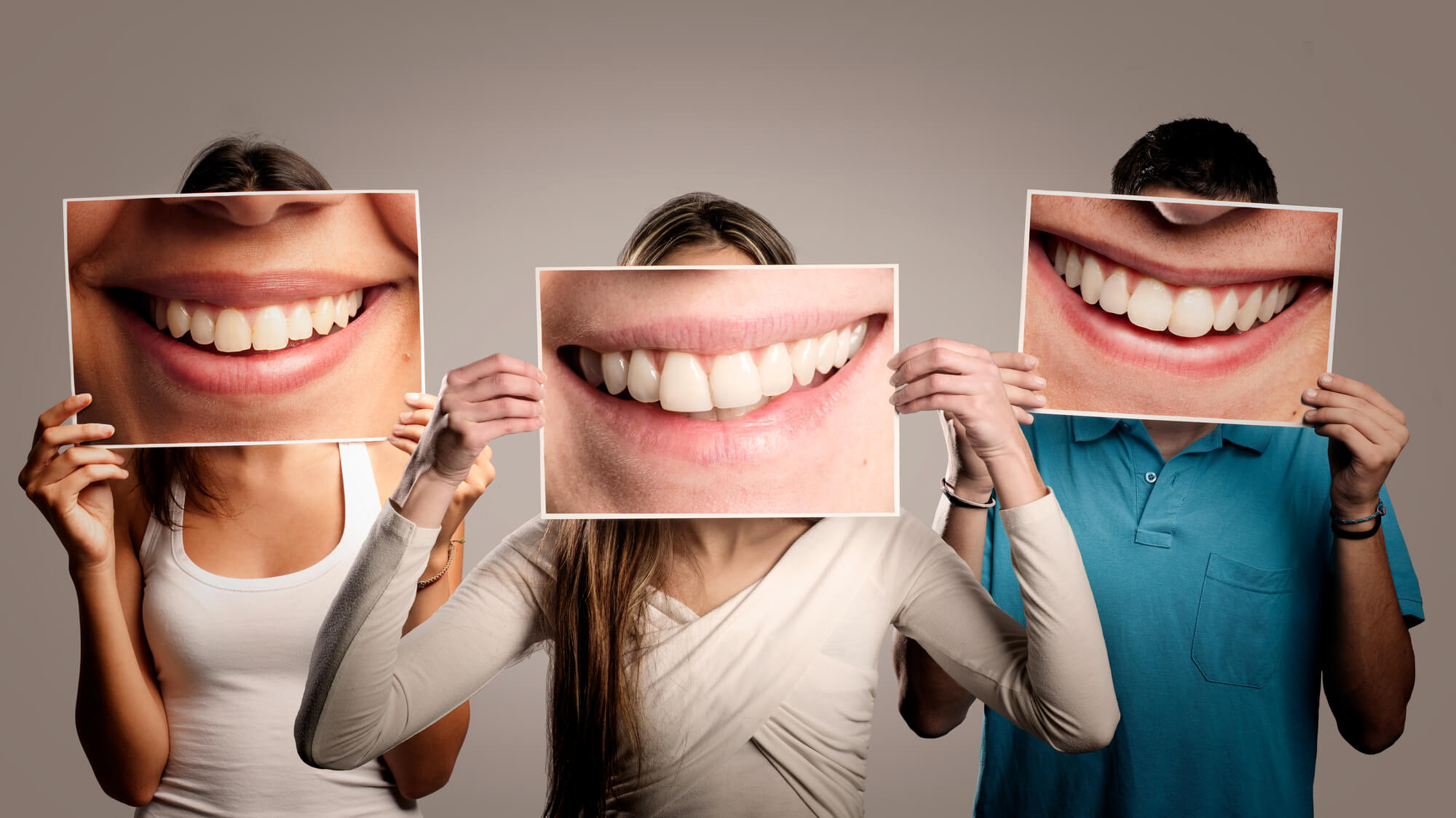 three happy dental patients holding photos of smiling mouths 