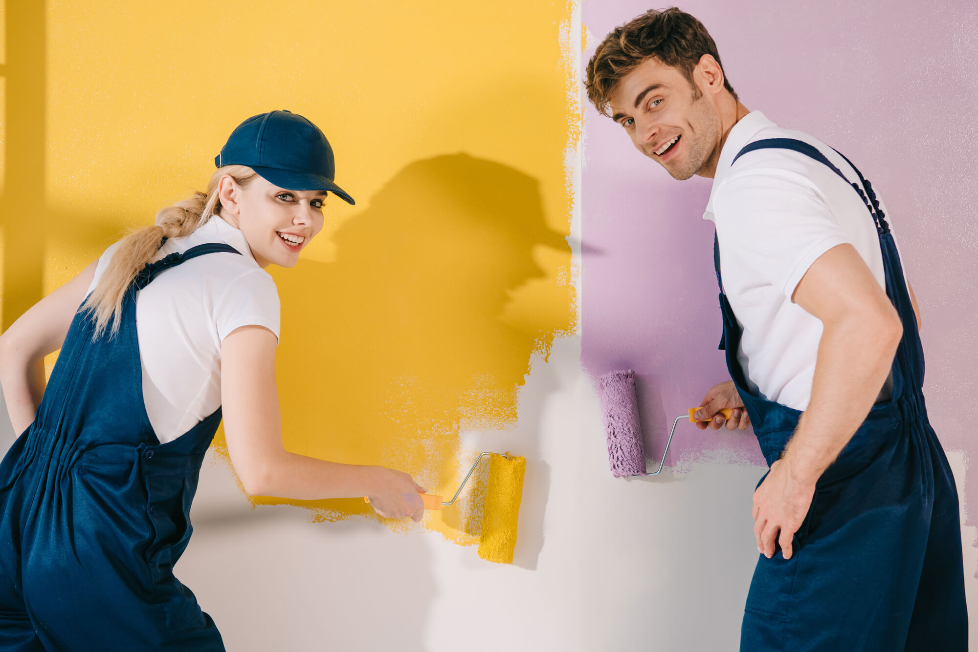 two painters smiling at the camera while painting a wall