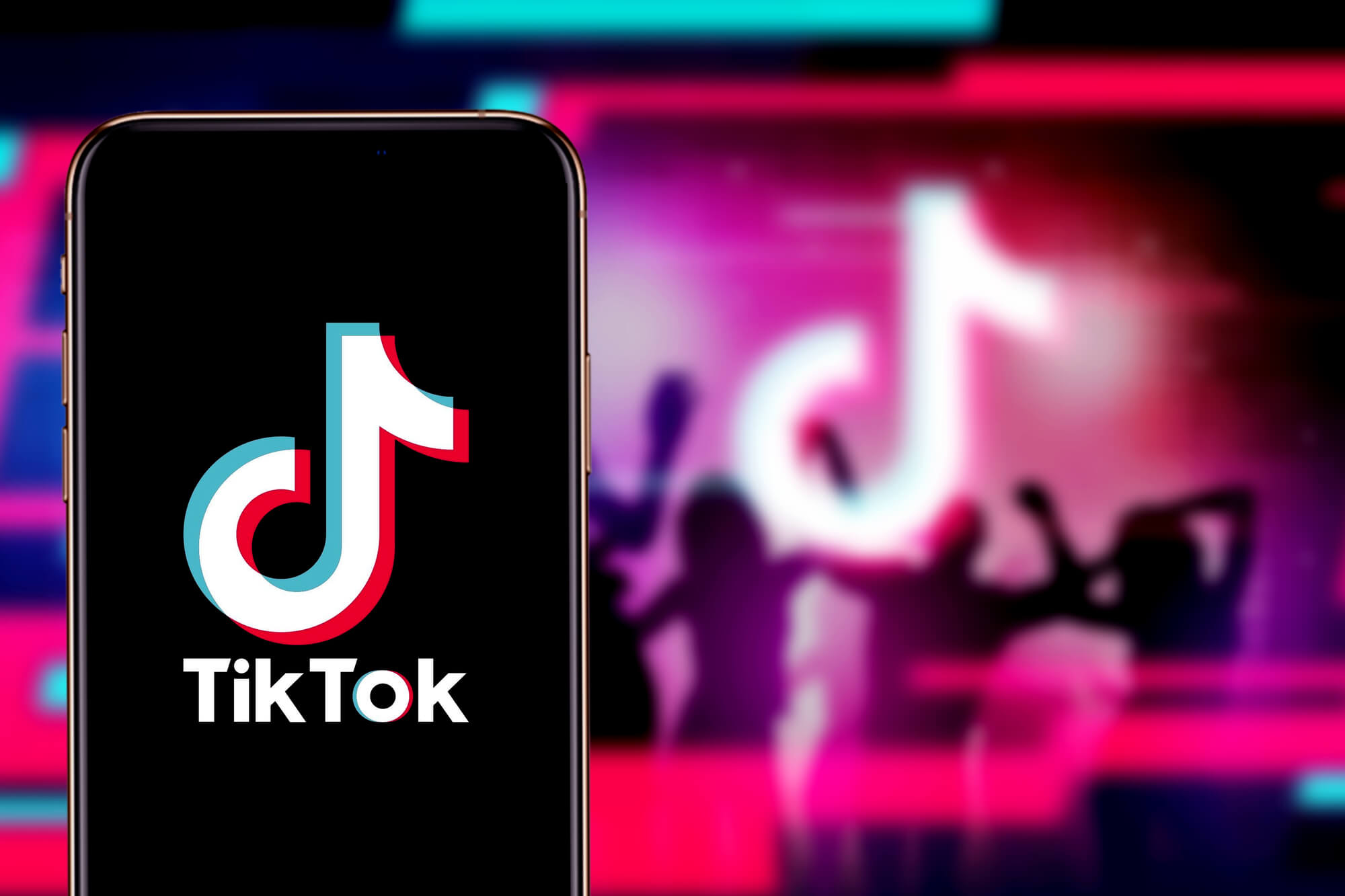 TikTok logo in a phone with silhouettes of dancing people in the background