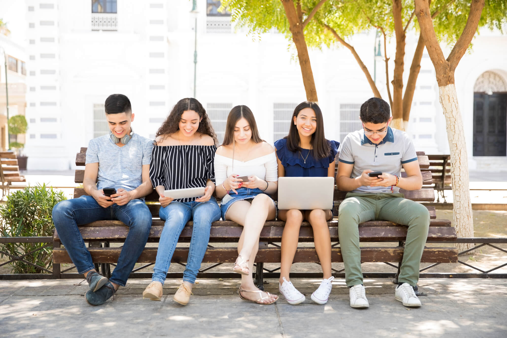 teens sitting on a bench with their gadgets