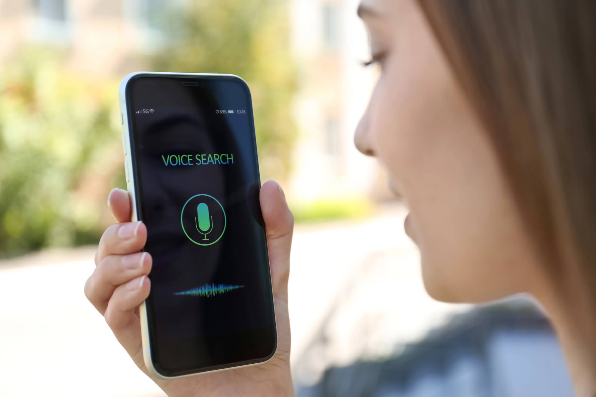 a woman holding a smartphone with "VOICE SEARCH" displayed while speaking into it