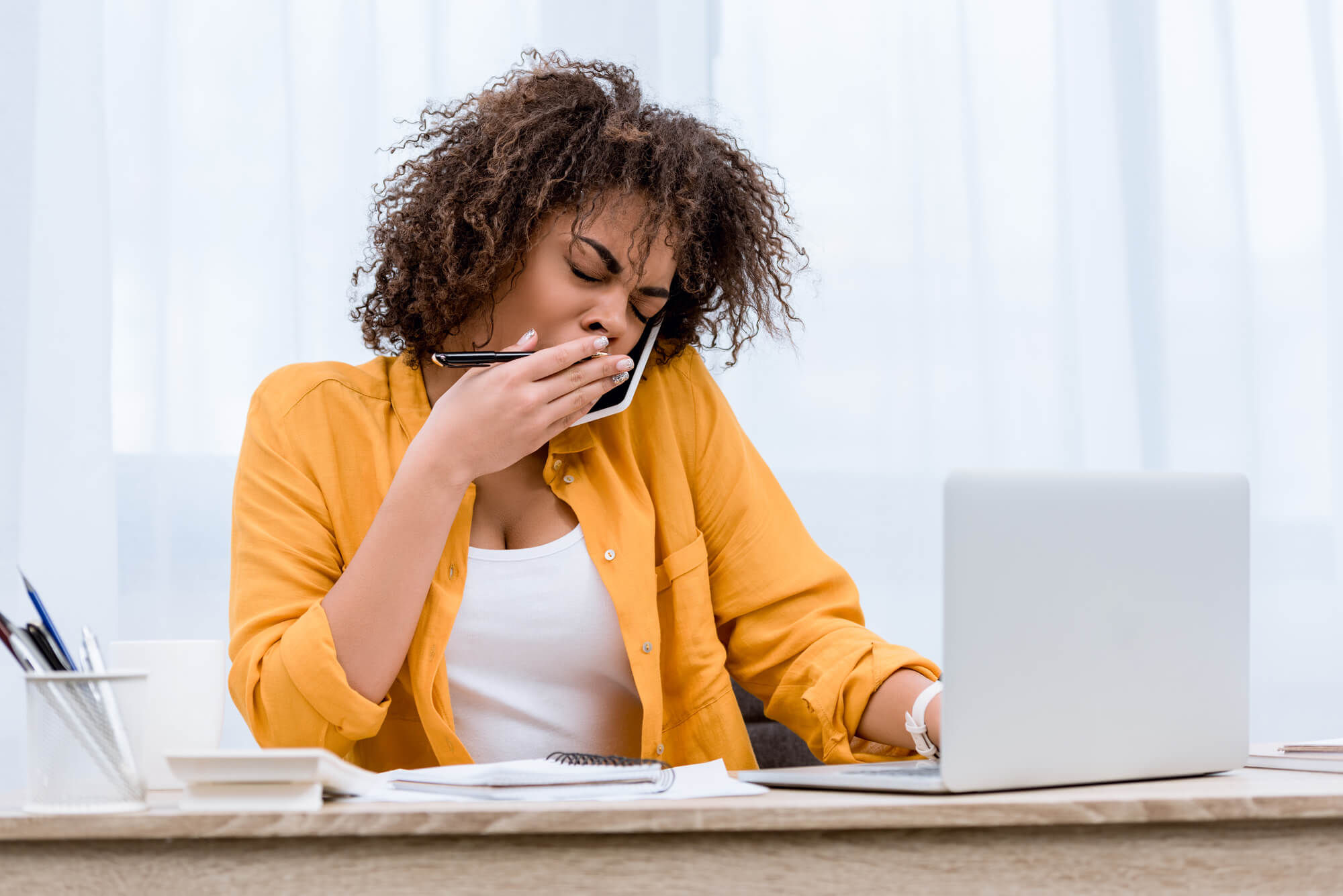 exhausted woman on the phone while trying to finish a report