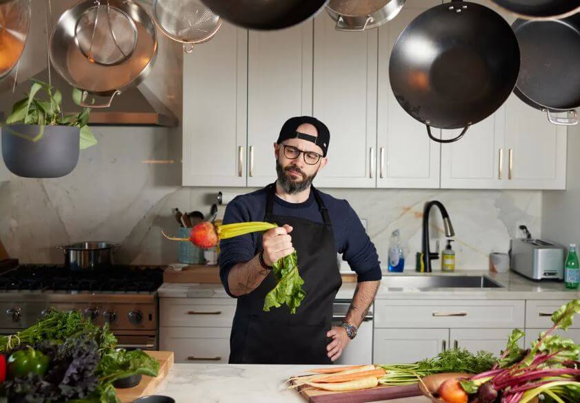 Photo of Andrew Rea holding a carrot in his kitchen studio.