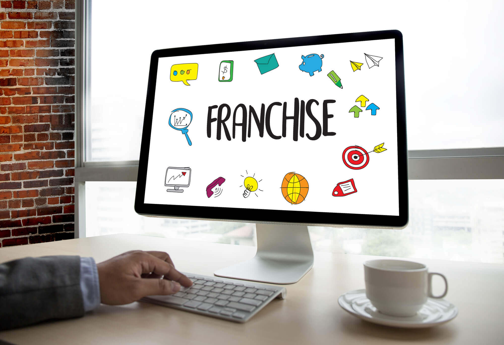 a professional's hand working on a computer with its screen displaying colorful marketing concept icons and the word FRANCHISE at the center