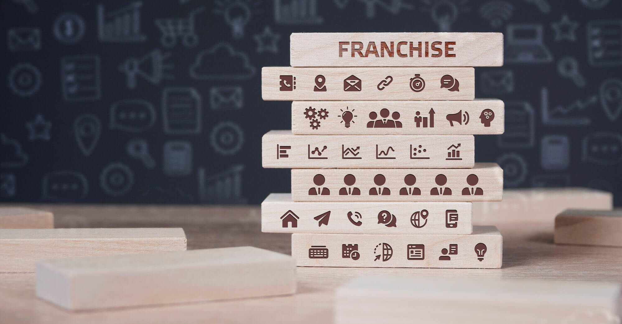 A stack of wooden blocks with various business icons and the word FRANCHISE on the top block 