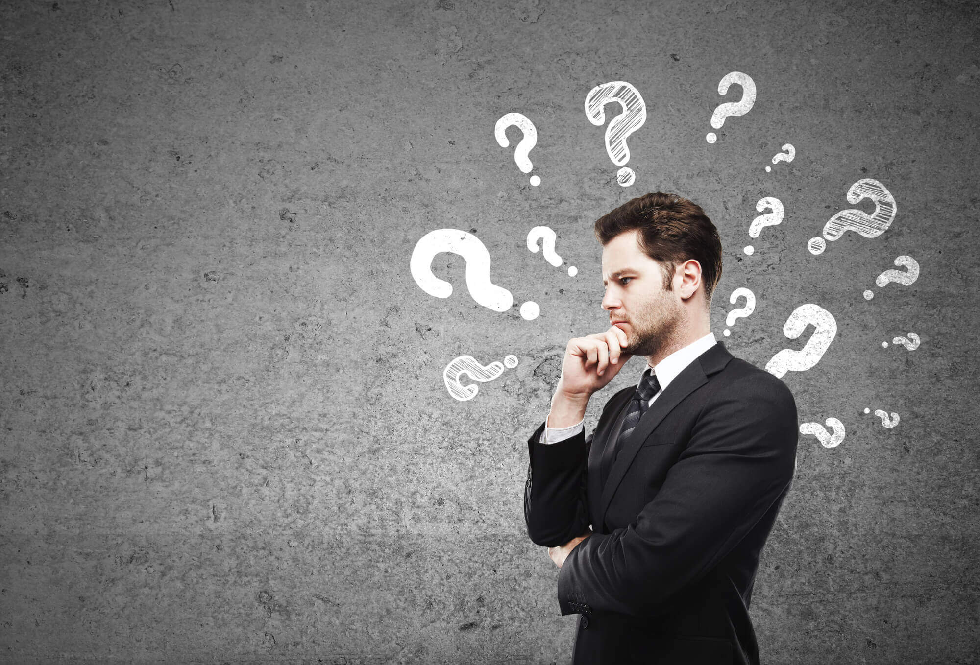 businessman in deep thoughts posing in front of a background with question marks  