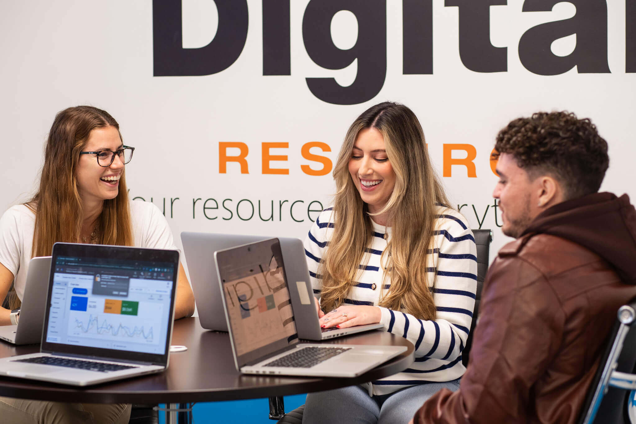 three DR paid advertising specialists working on their laptops while having a lighthearted chat