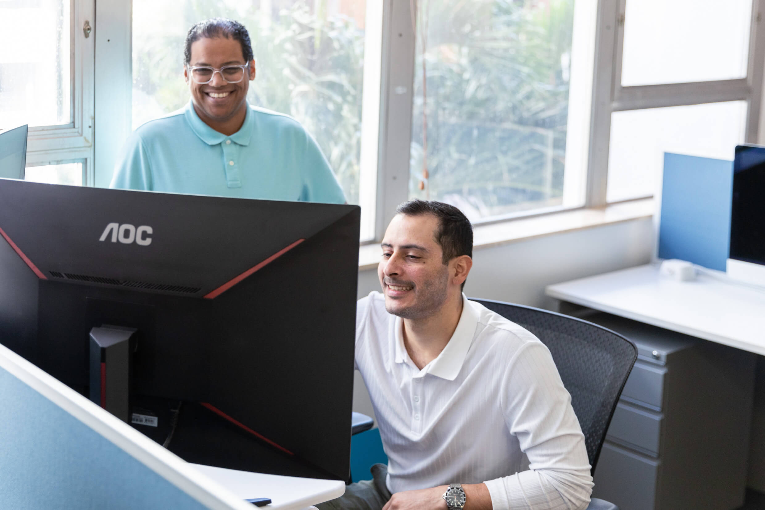 a marketer keenly working on his laptop and another standing and looking at the project with a smile 