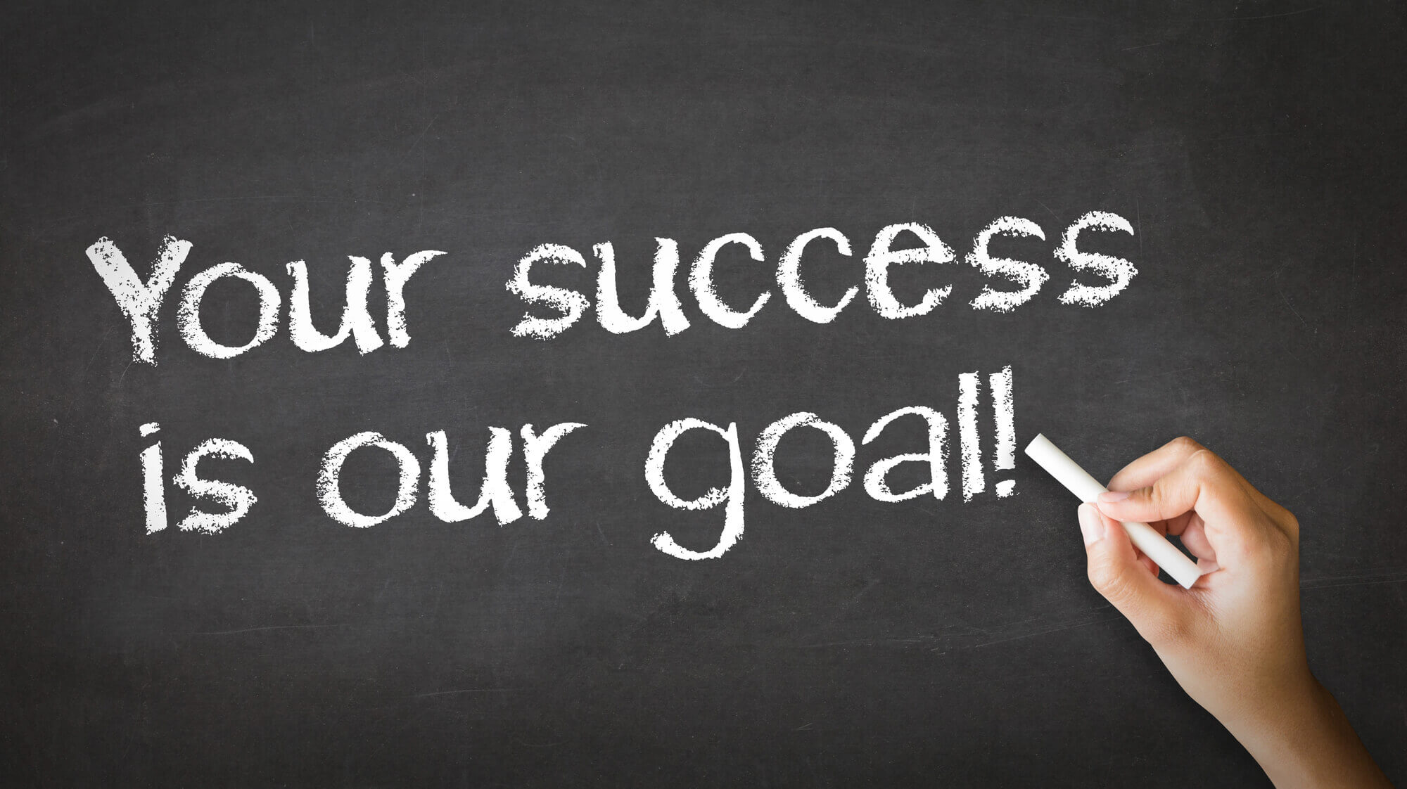 a hand writing YOUR SUCCESS IS OUR GOAL on blackboard
