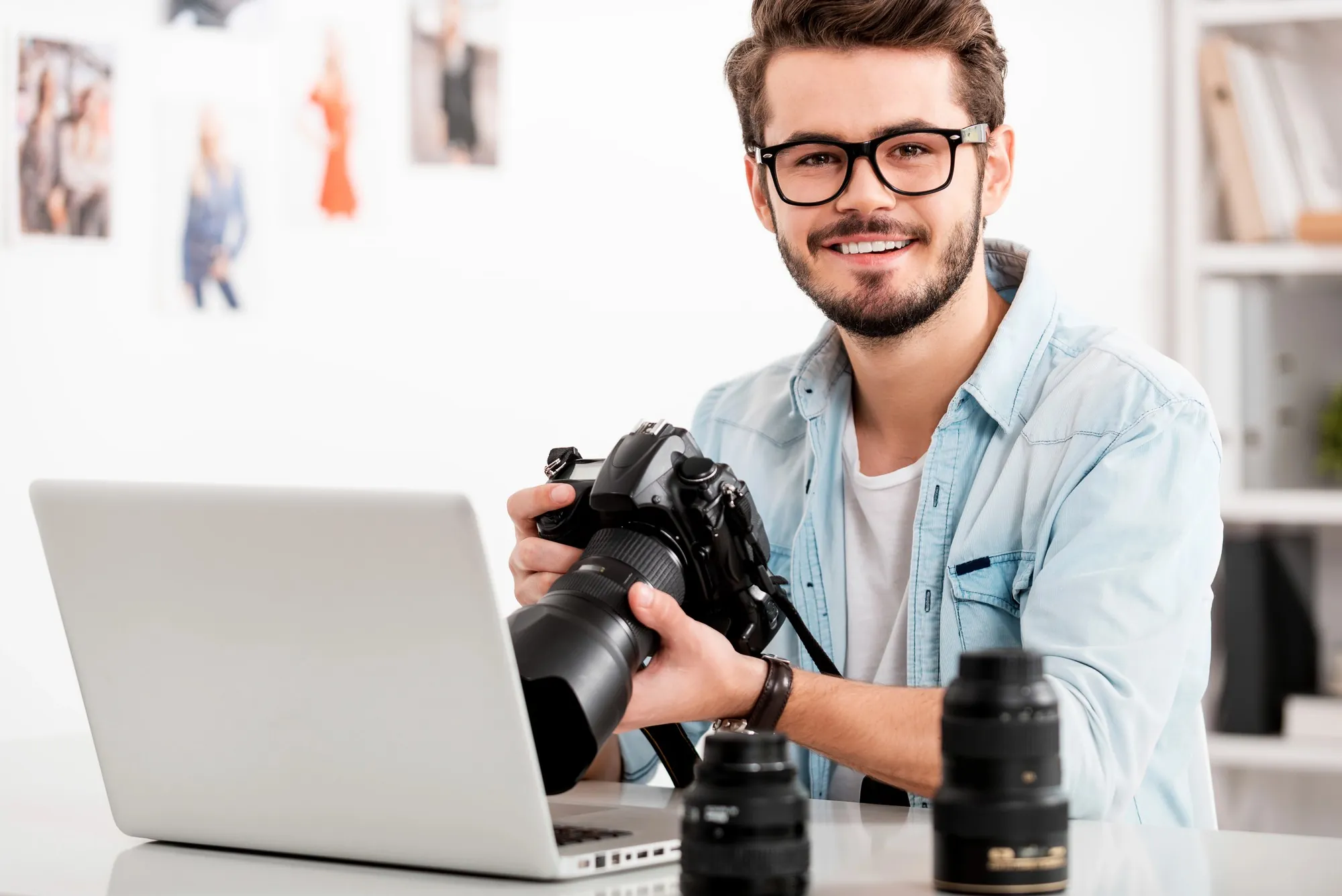 Professional photographer holding a DSLR camera while editing multimedia content on a laptop