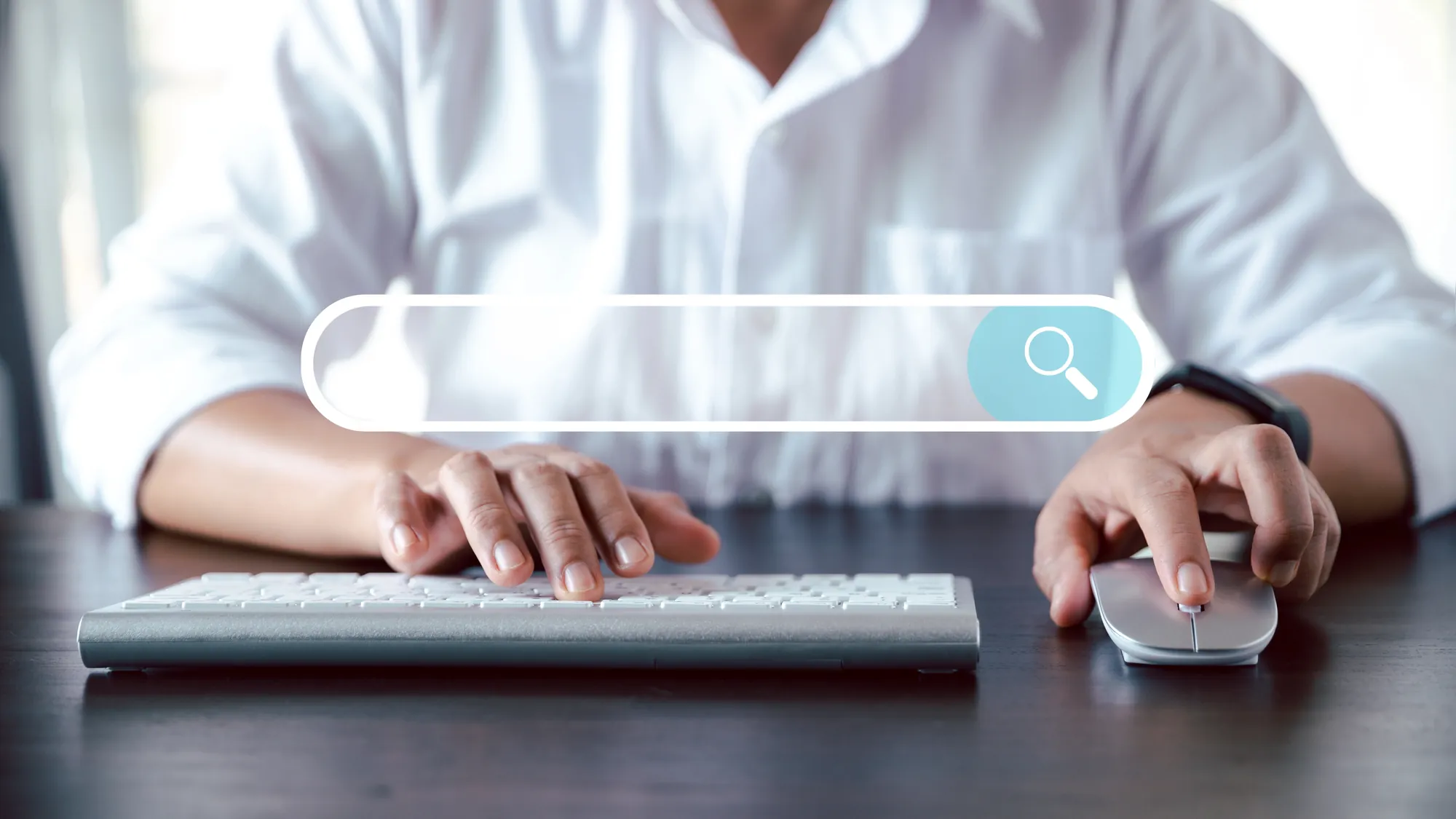 Person using a keyboard and mouse with a digital search bar and magnifying glass icon overlaid on the image