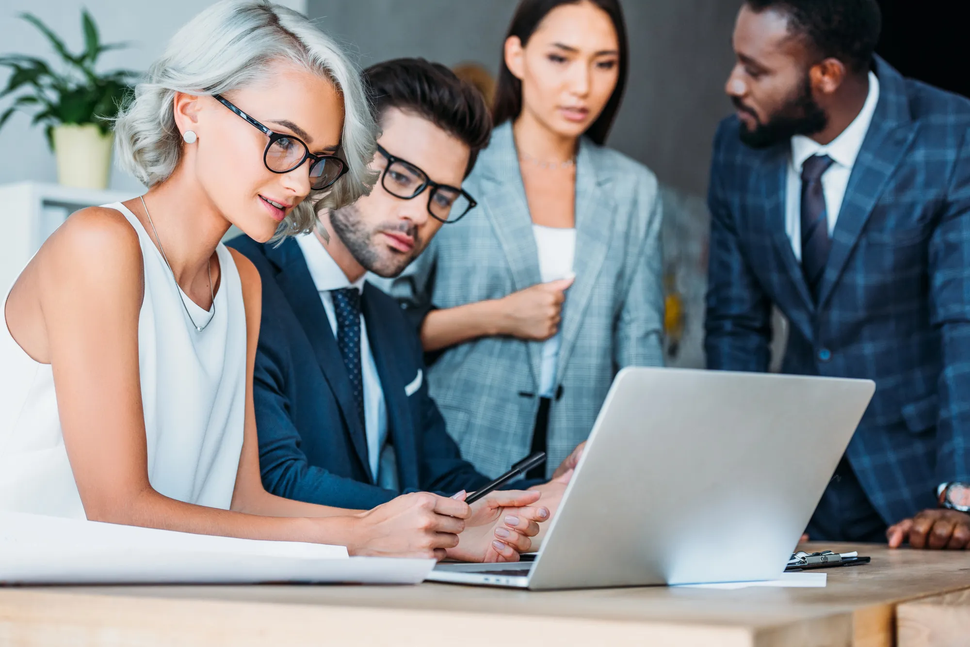 Diverse group of business professionals gathered around a laptop reviewing a document together in a modern office