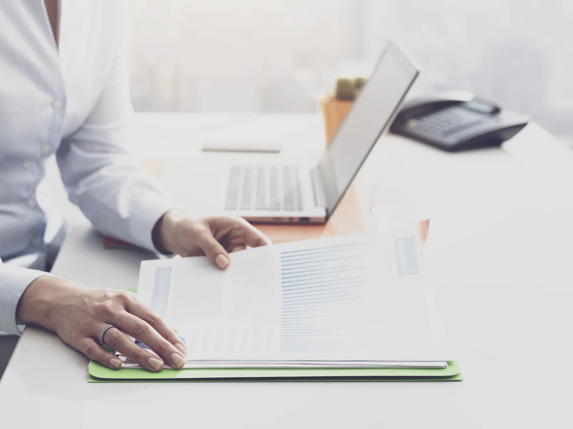Close-up of a hand reviewing a printed data report next to an open laptop on an office desk