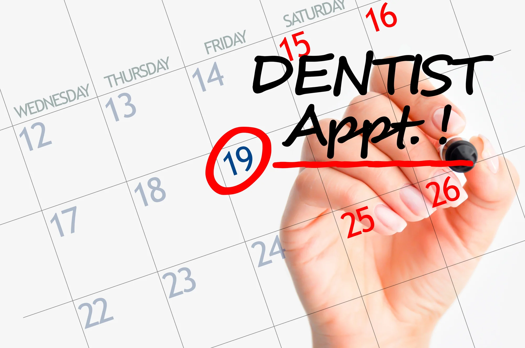 Hand circling a date on a calendar and writing Dentist Appt, representing a scheduled dental recall visit