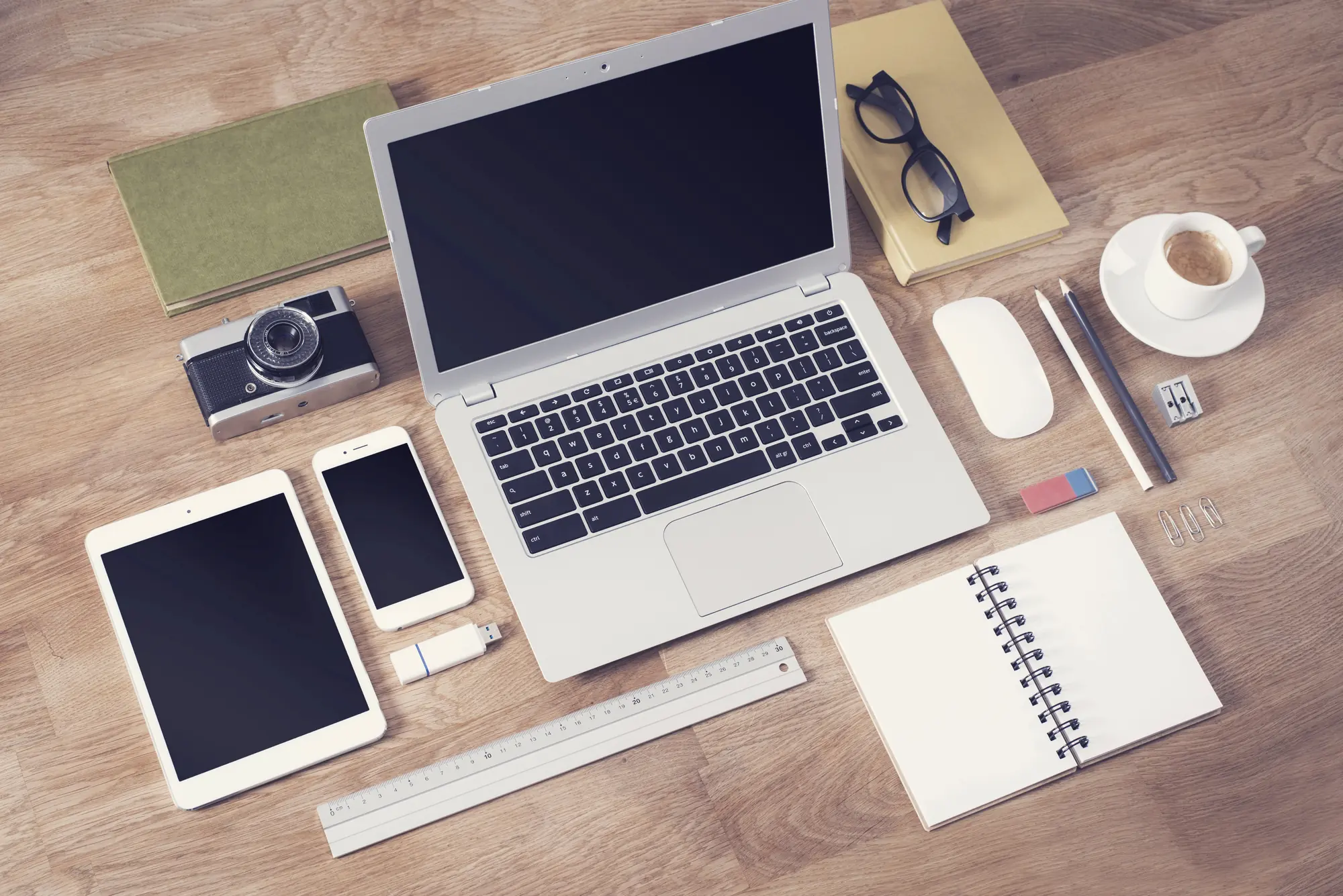 Overhead view of a designer's desk with an open laptop, tablet, smartphone, notebook, and camera for planning lead generation website design