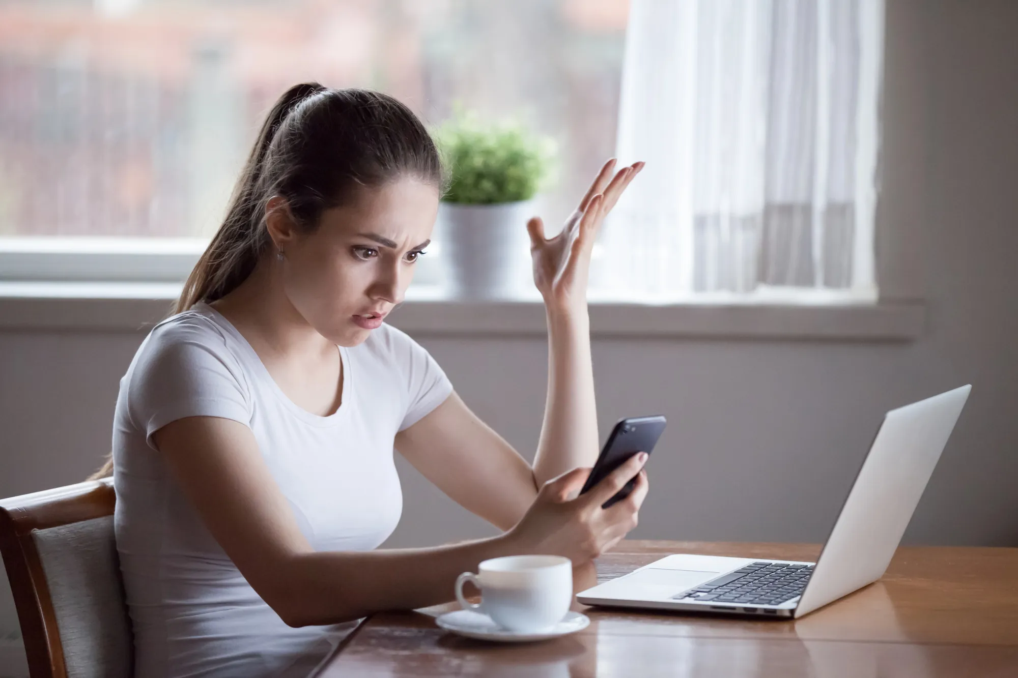 Frustrated business owner staring at her phone beside a laptop after a traffic drop, showing why SEO audit services matter after a Google spam update