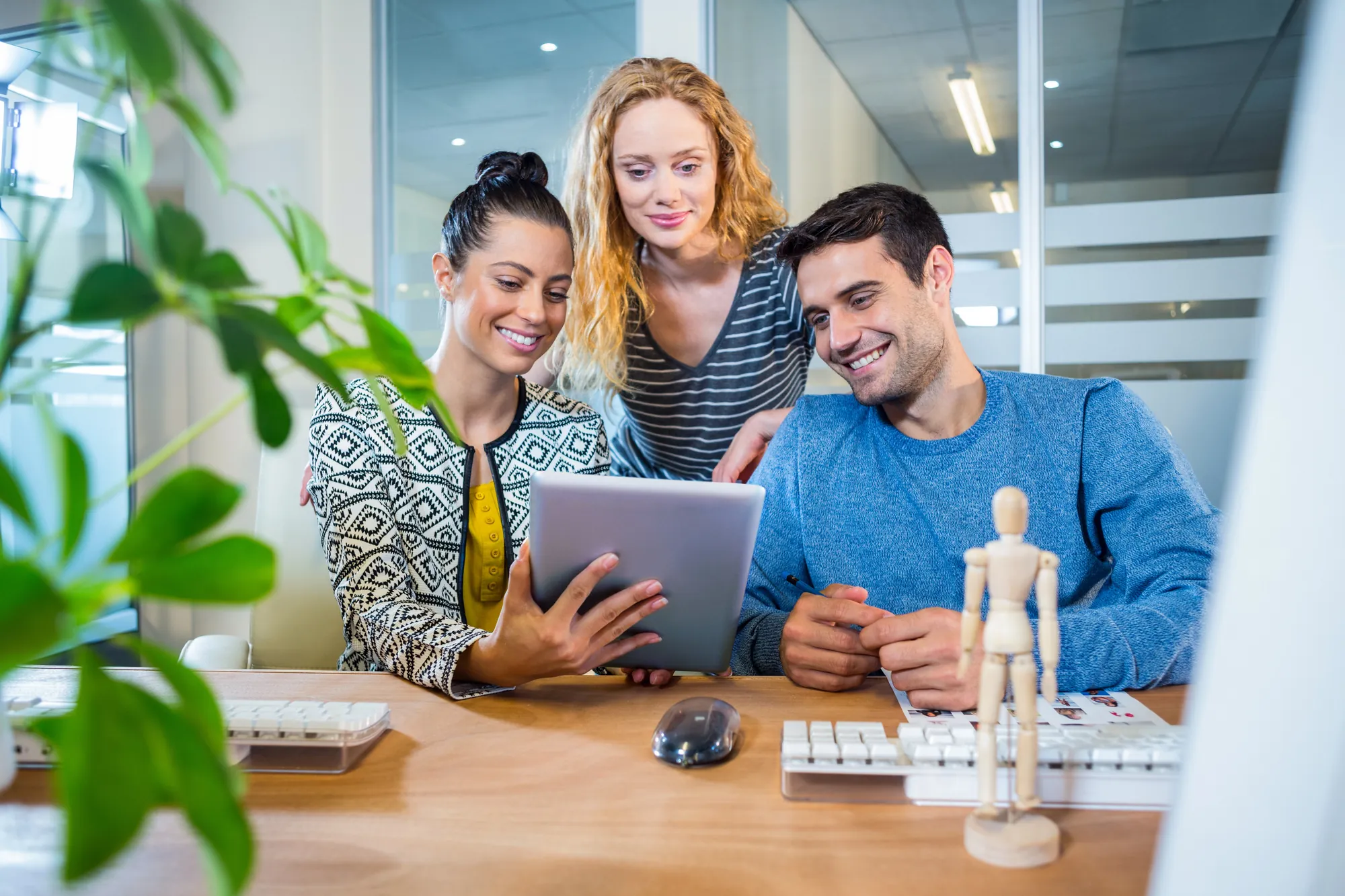 Marketing team of three smiling while reviewing results on a tablet at an office desk, illustrating collaborative planning for LLM optimization