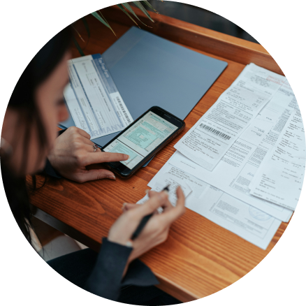 Person managing finances with smartphone and documents at wooden desk.