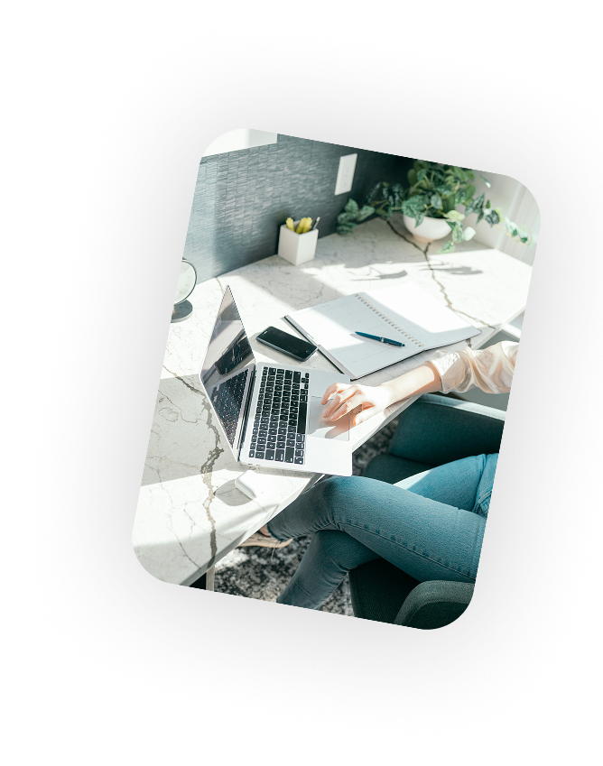 Two people working on a laptop at a bright office desk.