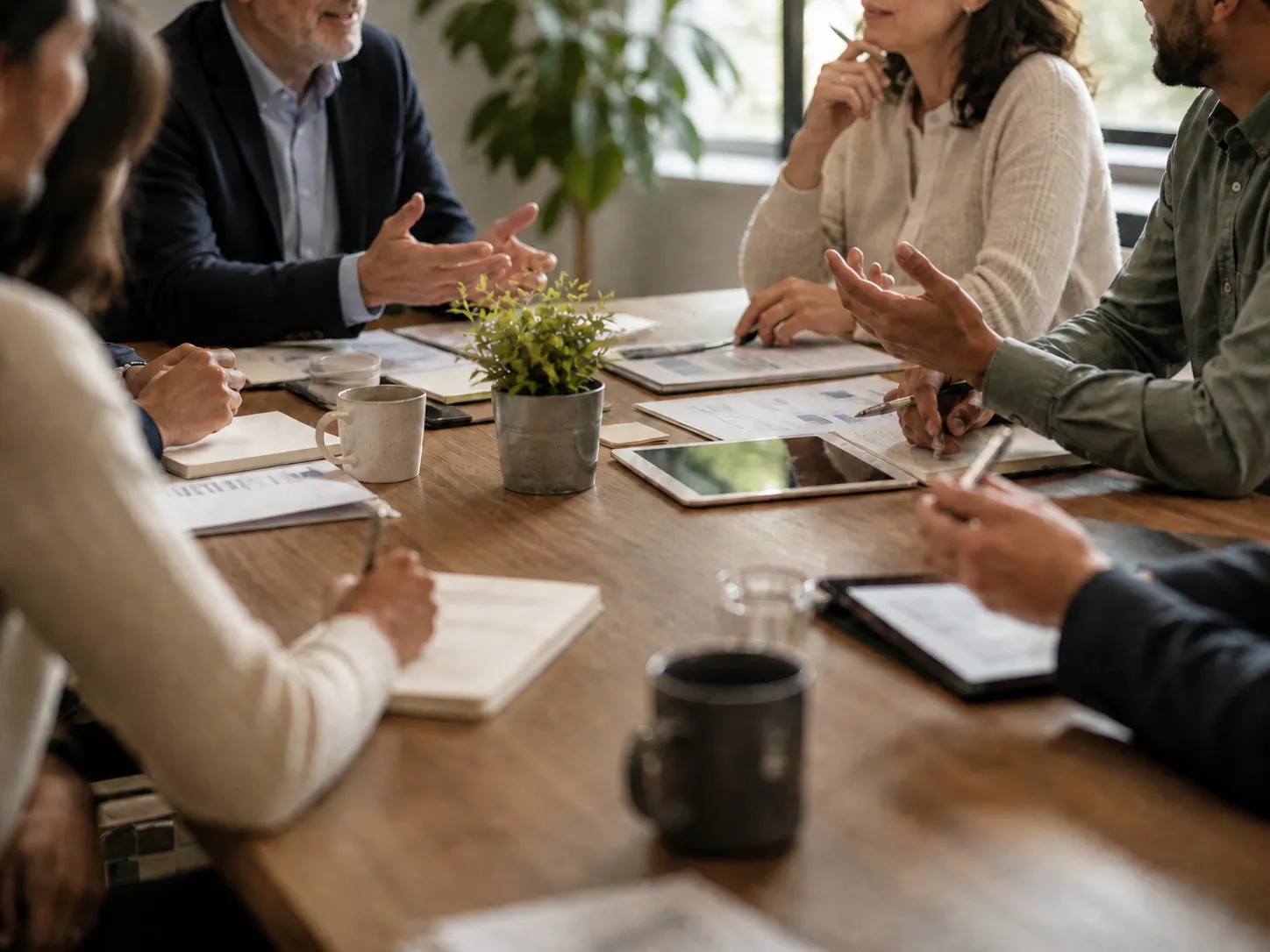 People sitting around a wooden table in a meeting, discussing documents and using tablets.