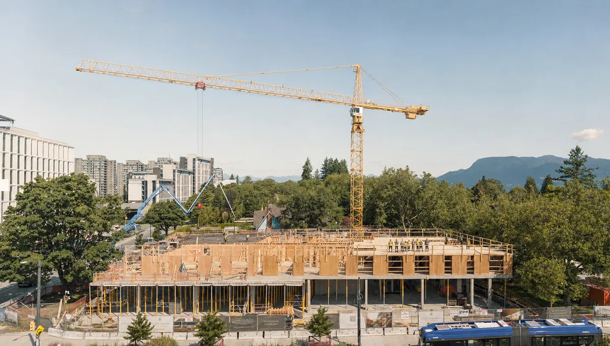 Construction site with a large crane and workers on the wooden framework of a building.