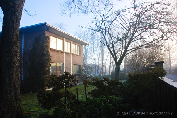 Two-story brick building with large windows surrounded by trees and shrubs on a foggy morning.
