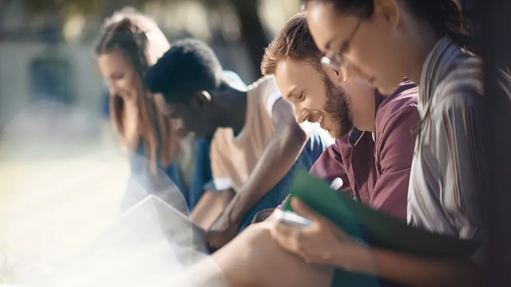 Group of young diverse people sitting outdoors and reading books together in daylight.