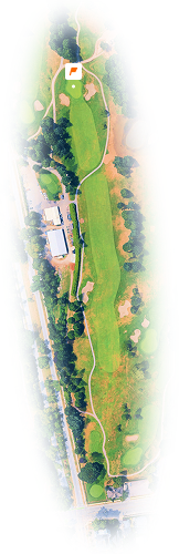 Aerial view of a golf course hole with fairways, bunkers, greens, trees, and a nearby building.