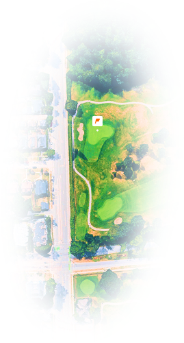 Aerial view of a golf course hole adjacent to residential homes and roads, showing sand traps and green fairways.