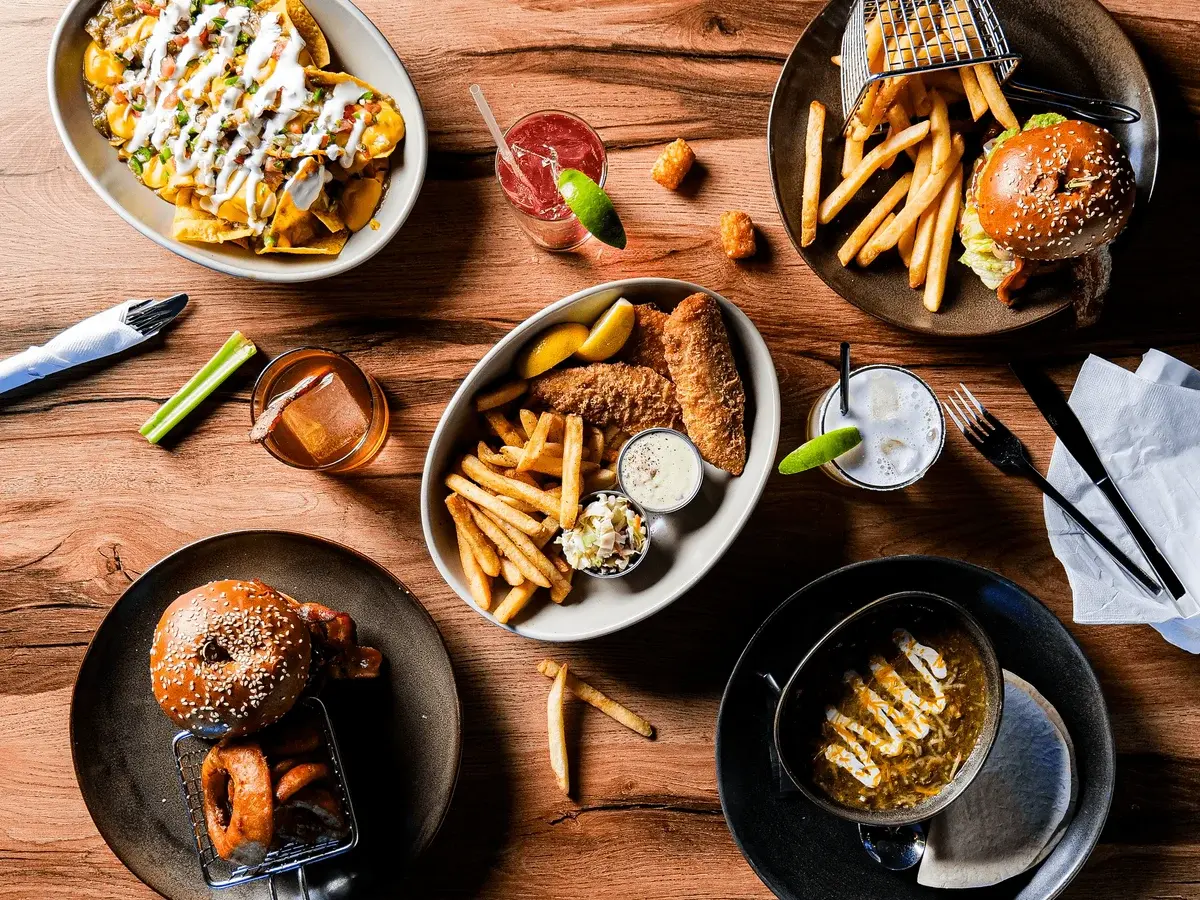 A spread of delicious food including nachos, burgers, fries, and drinks on a wooden table.