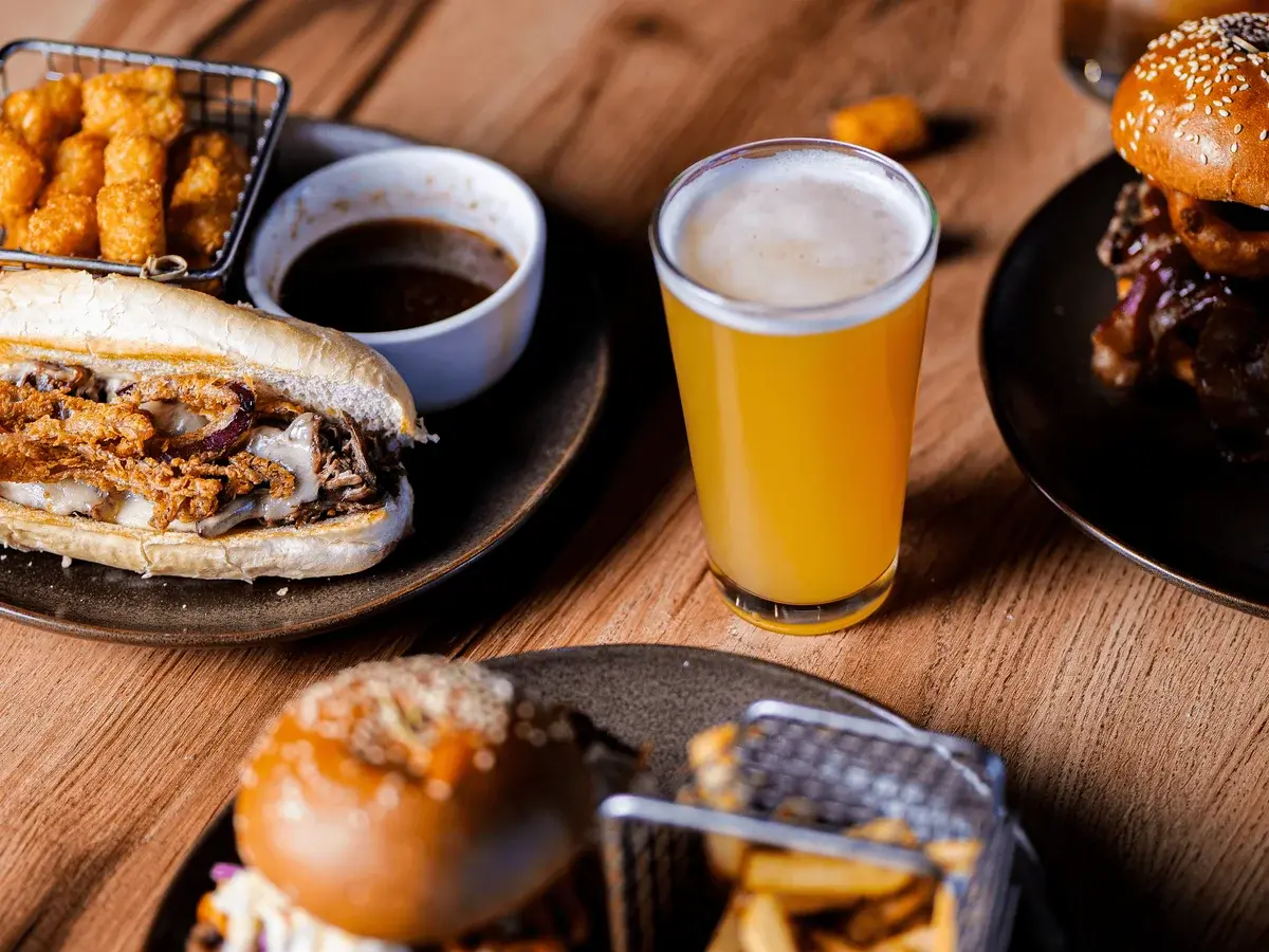 A selection of delicious food items, including a sandwich, tater tots, and a glass of beer on a wooden table.