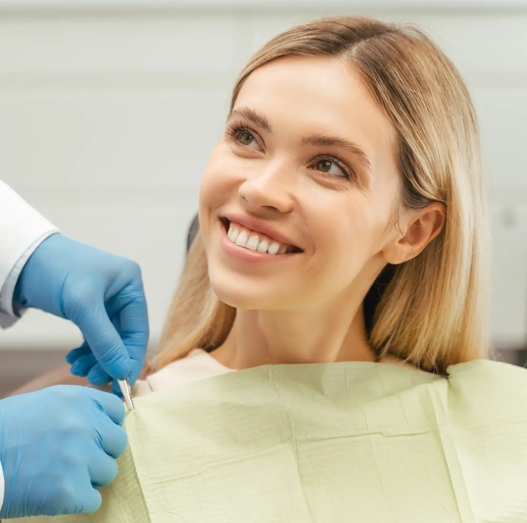 Smiling woman with dental bib, thumbs up by a dentist wearing blue gloves.