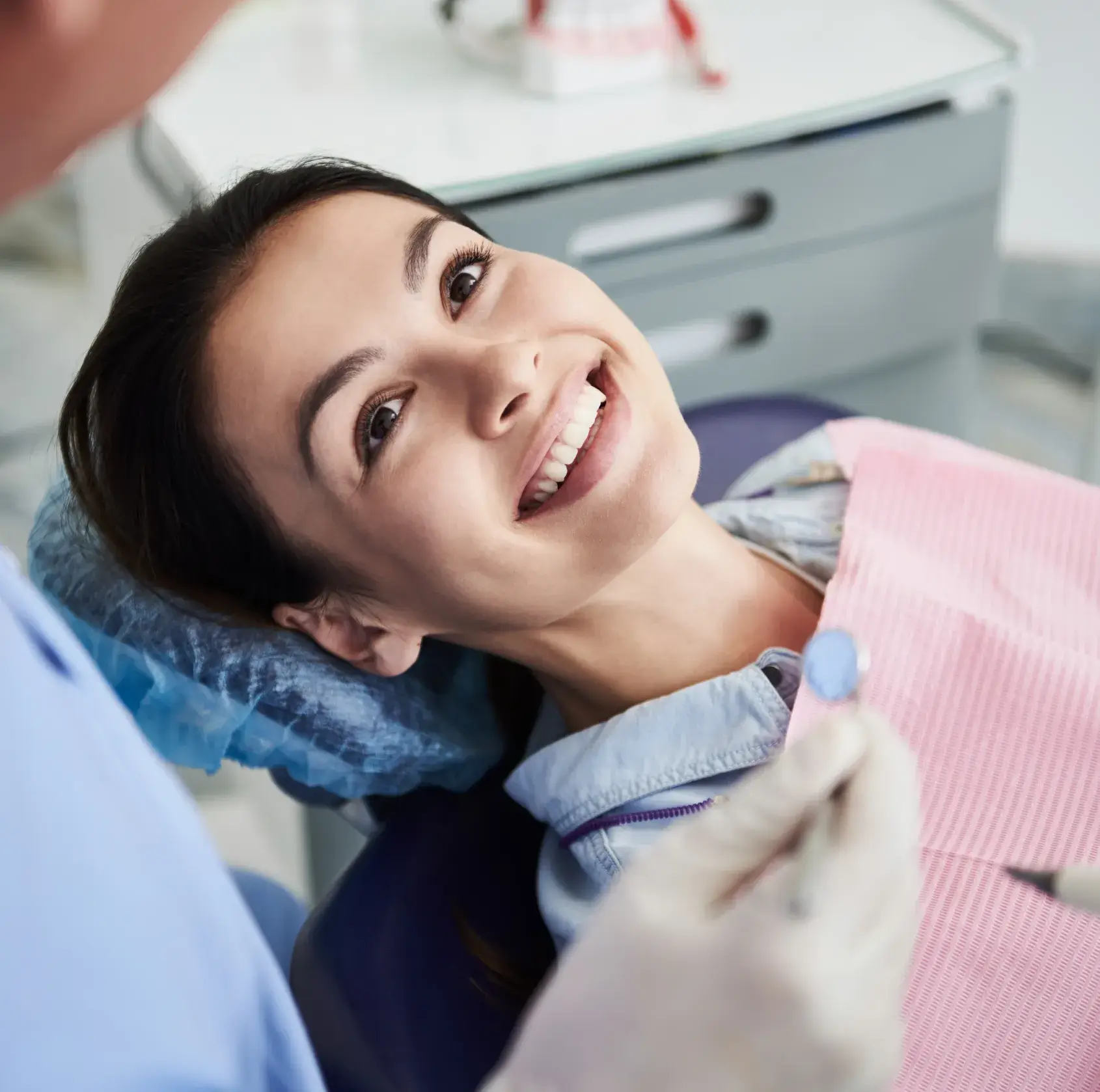 Woman reclining in dental chair smiling at dentist holding dental mirror during checkup.