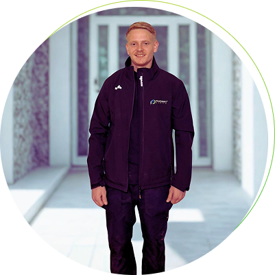 Smiling man with short blond hair wearing a black jacket and pants standing in a modern hallway.