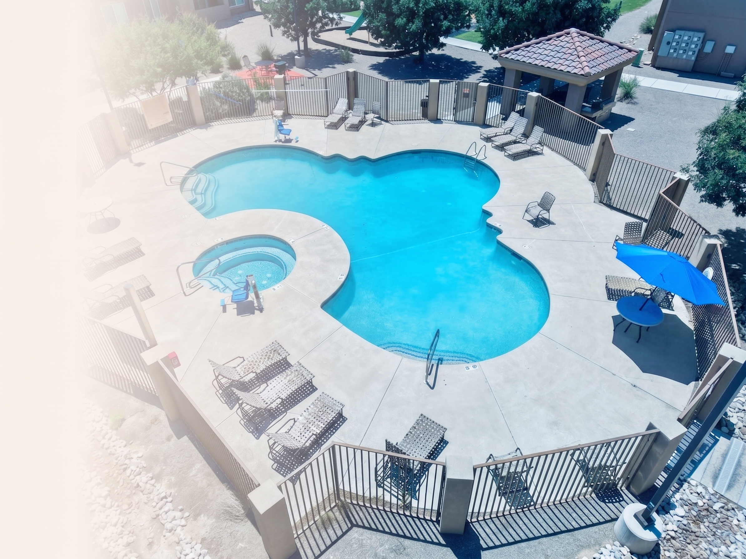 Outdoor swimming pool with lounge chairs and a building in the background under a cloudy sky.