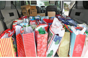Multiple colorful gift bags with various holiday patterns, including stripes and Christmas trees, arranged inside the back of a vehicle.