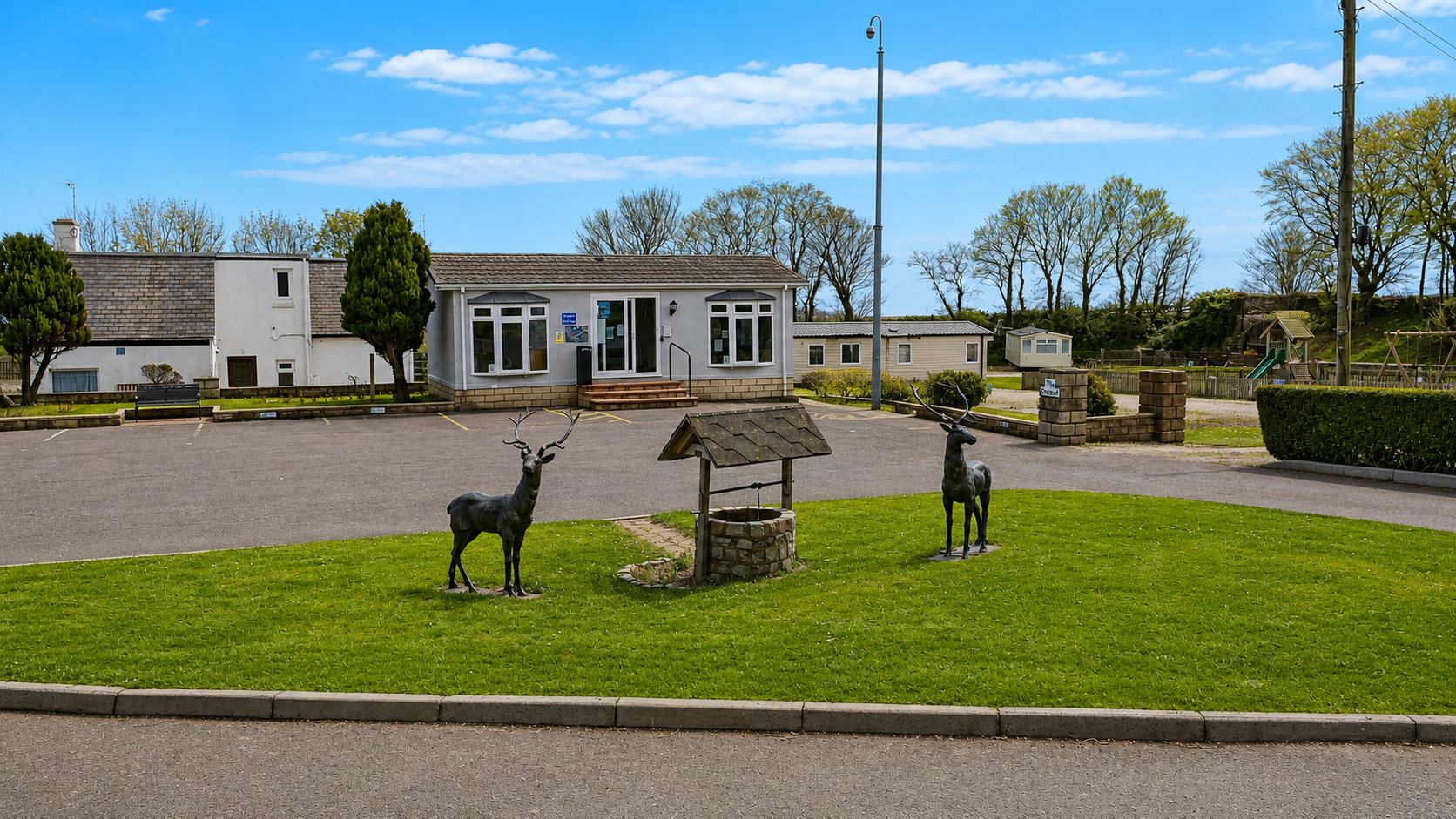 Caravan park with modern facilities, metal deer statues, and wishing well on green lawn