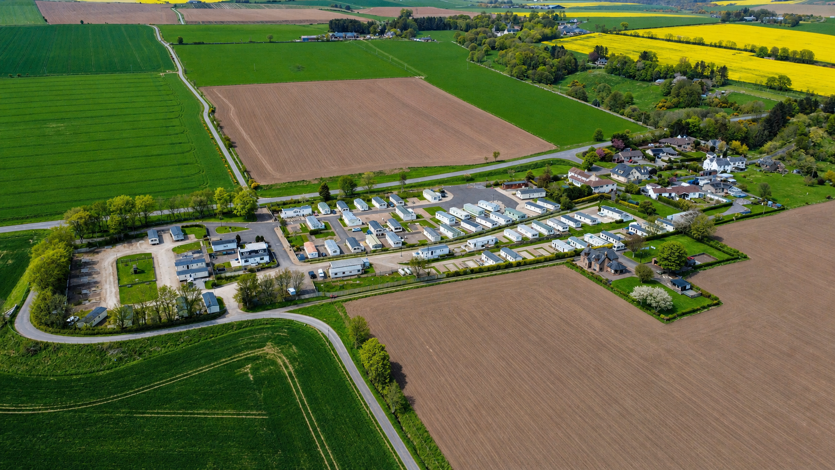 Aerial view of rural residential community surrounded by green and brown agricultural fields