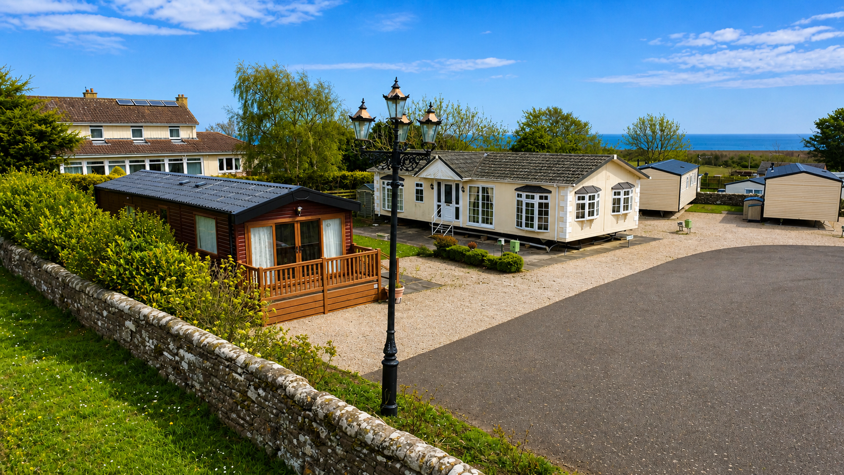 Luxury holiday park with cream caravans, wooden lodge, and ocean view under blue sky