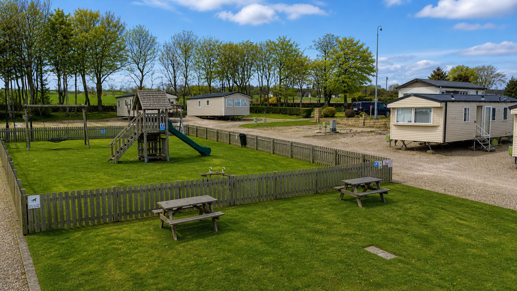Mobile home holiday park with caravans, playground, picnic tables, and green lawns