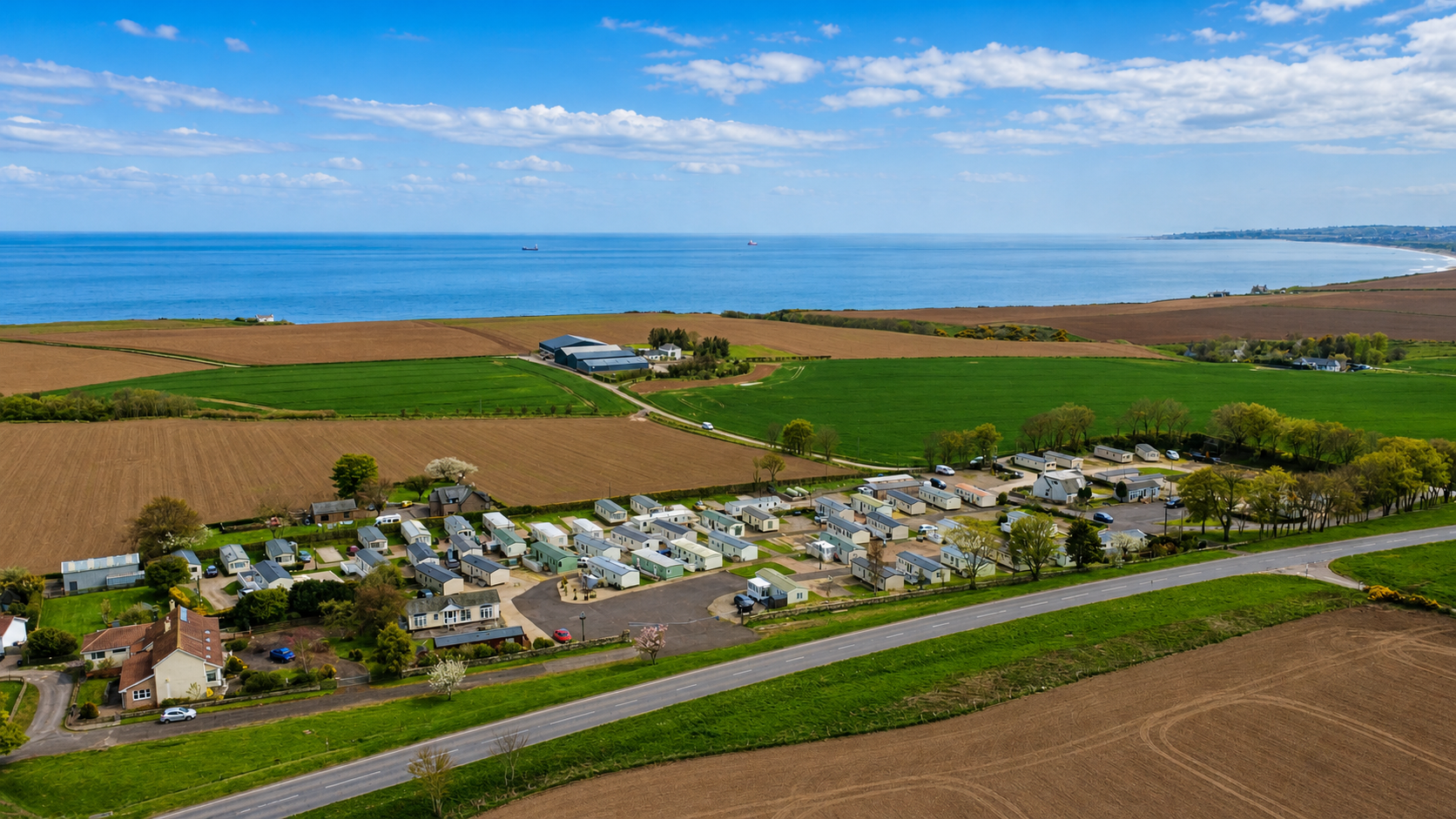 Aerial view of seaside caravan park with blue ocean, farmland, and coastal countryside.