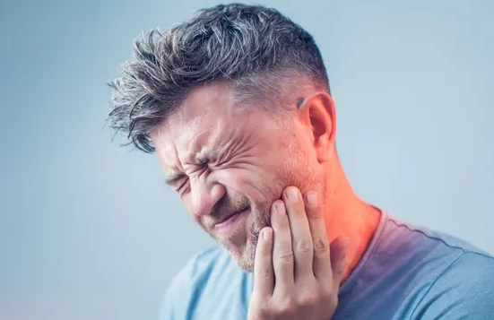 Man grimacing in pain holding the right side of his jaw and neck.